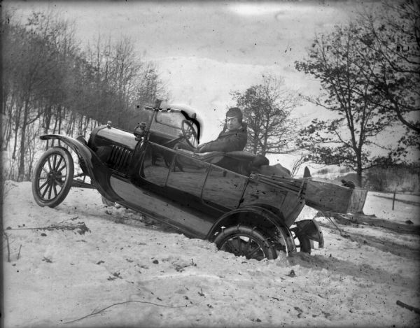 An ol' timey car with its back tyres half-buried in snow, so it kinda looks like the car is doing a wheely.